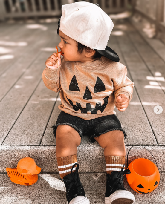 Toddler wearing a neutral pumpkin Halloween sweatshirt with jack-o-lantern face graphic, perfect for fall and Halloween outfits.
