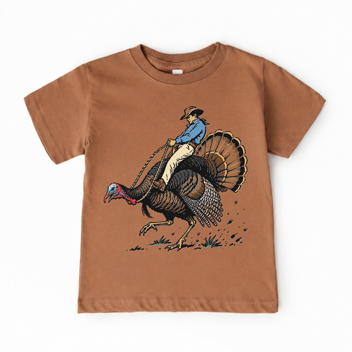 A toddler's brown short-sleeve t-shirt featuring a graphic print of a cowboy riding a running turkey, shown against a plain white background.